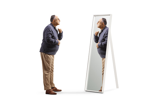 Full length profile shot of a mature man getting ready and looking at a mirror isolated on white background