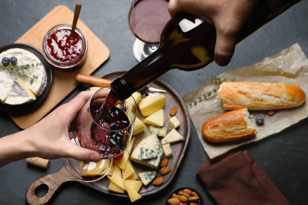 uomo che versa vino rosso dalla bottiglia nel bicchiere sopra il tavolo nero con snack, vista dall'alto - wine bottle bottle burgundy wine foto e immagini stock