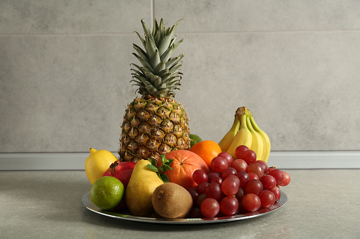 Plate with different ripe fruits on grey table