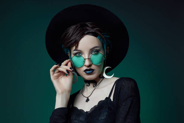 Woman in a round hat and green round glasses on a green dark background Woman in a round hat and green round glasses on a green dark background. goth stock pictures, royalty-free photos & images