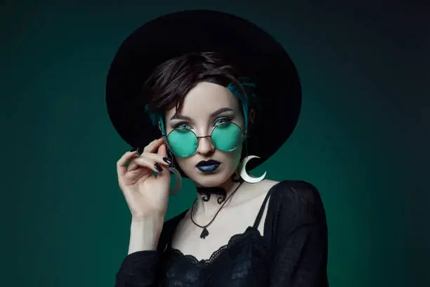 Woman in a round hat and green round glasses on a green dark background.