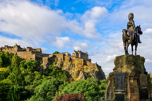Edinburgh,  UK - July 12, 2022 : The Royal Scots Greys Monument statue in Princes Street Gardens, with Edinburgh Castle in the background. The statue was sculpted by William Birnie Rhind, was unveiled in 1906.