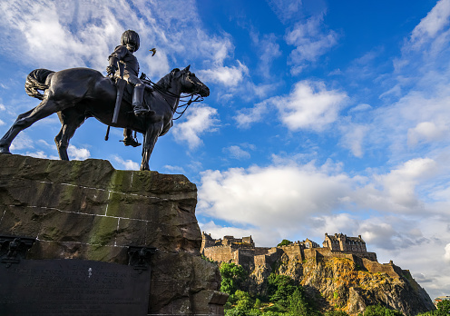 Edinburgh,  UK - July 12, 2022 : The Royal Scots Greys Monument statue in Princes Street Gardens, with Edinburgh Castle in the background. The statue was sculpted by William Birnie Rhind, was unveiled in 1906.