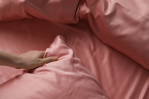 Mujer haciendo la cama con hermosas sábanas de seda rosa, vista de cerca photo