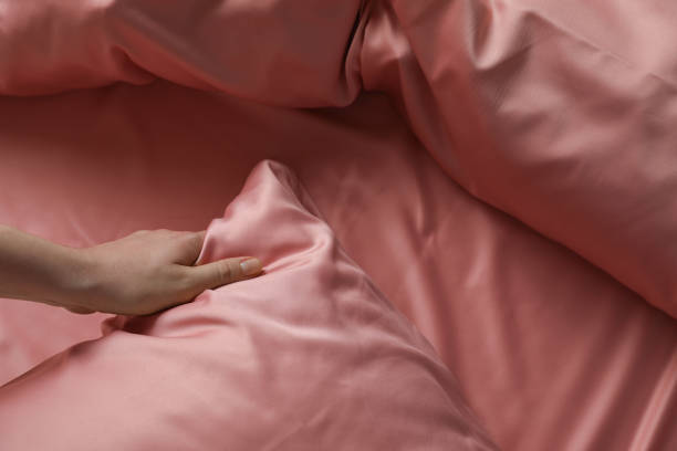 женщина заправляет постель с красивым розовым шелковым постельным бельем, вид крупным планом - шелк стоковые фото и изображения