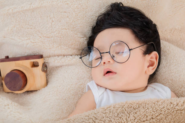 asian newborn baby wearing glasses sleeping with beige blanket next to toy camera with safe and comfortable. adorable baby resting after eat full. little toddler cute sleeping sweet dreams. - 5943 imagens e fotografias de stock