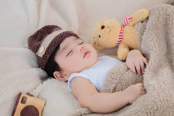 азиатский очаровательный новорожденный ребенок носит коричневую вязаную шапку, глубоко спящую с бежевым одеялом рядом с плюшевым мишкой и - 5956 стоковые фото и изображения