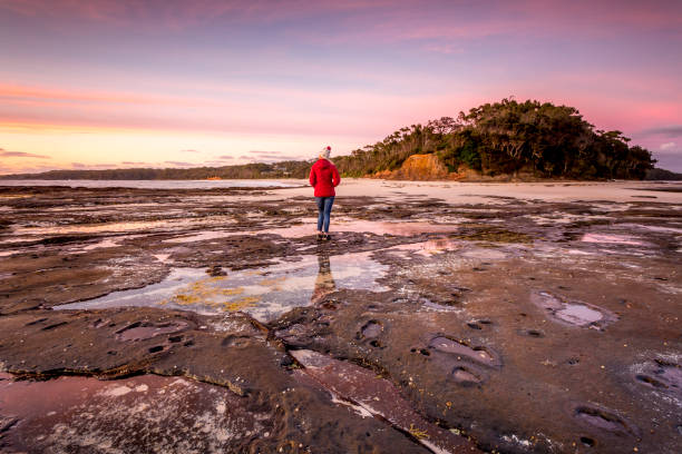 istock Woman watching the sunrise from the outer rocky reef 1423019871