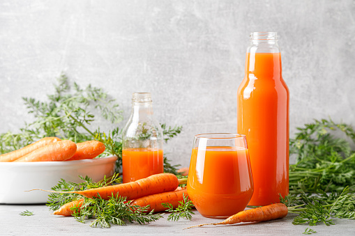 Carrot juice in a glass and bottle and fresh carrots with leaves