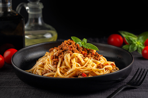 Italian dinner with Spaghetti or linguine with meat and tomato sauce bolognese on a black plate and dark background. Copy space.