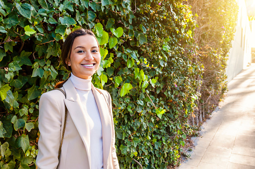Multiracial businesswoman with a wall of green leaves in the background - stylish young woman smiling at city