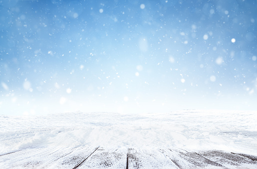 defocused winter background with snowfall and snow covered empty wooden walkways
