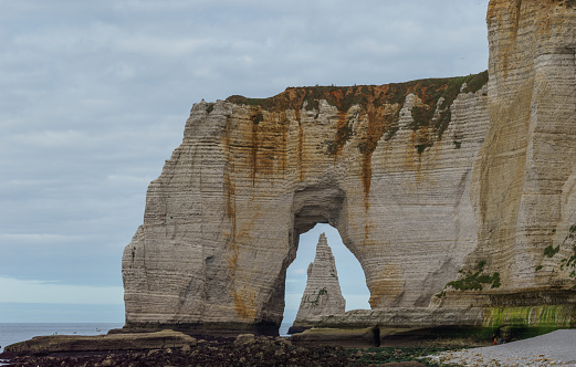 The Needle seen through the arch of the Manneporte cliff at the Alabaster coast on a cloudy summer day, Etretat, Normandy, France