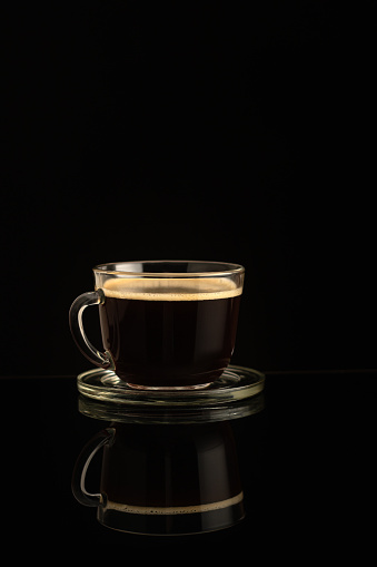 Glass cup of fresh fragrant coffee on a dark background. Reflection of a cup on a glass surface.