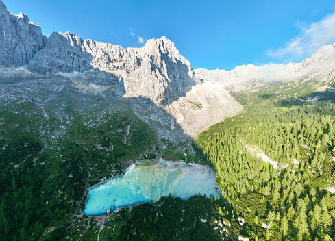 View from above, stunning panoramic view of the Lake Sorapis (Lago di Sorapis) with its turquoise waters surrounded by a forest and beautiful rocky mountains.  Aerial shot, Dolomites, Italy.