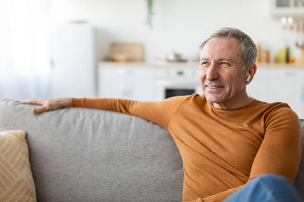 Calm mature man having rest at home listening to music Closeup Portrait Of Happy Mature Man Listening To Music Wearing Wireless Earphones Looking Away Sitting On Couch At Home. Senior Male Relaxing Resting On Sofa Enjoying Favorite Song, Thinking Dreaming old person listening to radio stock pictures, royalty-free photos & images