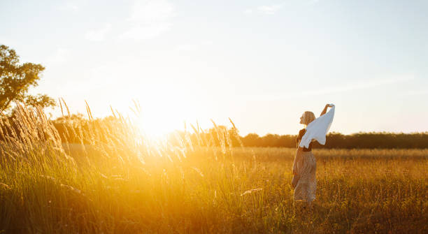 istock Peaceful young blond woman standing amidst wheat field. Against setting sun 1423053076