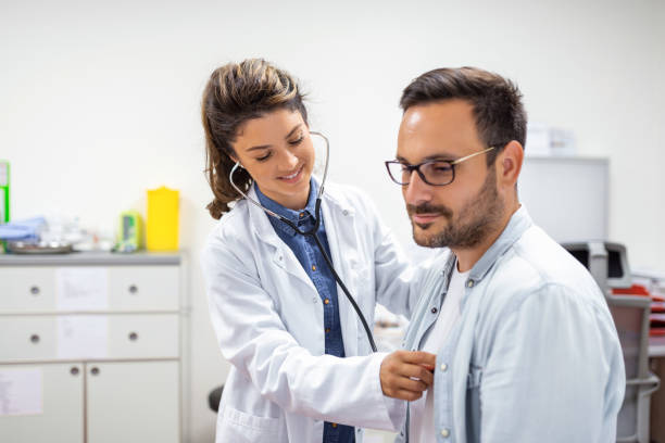 젊은 의사는 청진기를 사용하여 환자의 심장 박동을 듣고 있습니다. 남성 환자에게 검진을주는 여성 의사의 샷 - medical check 뉴스 사진 이미지