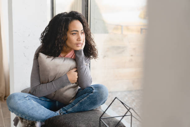 Depressed pensive thoughtful african young woman housewife suffering from periods pain headache coronavirus migraine broken heart looking outside on windowsill at home on self-isolation