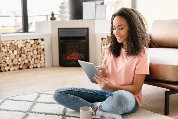 istock Happy young african woman using digital tablet, surfing social media, e-learning, working on distance relaxing on the floor at home 1423054454