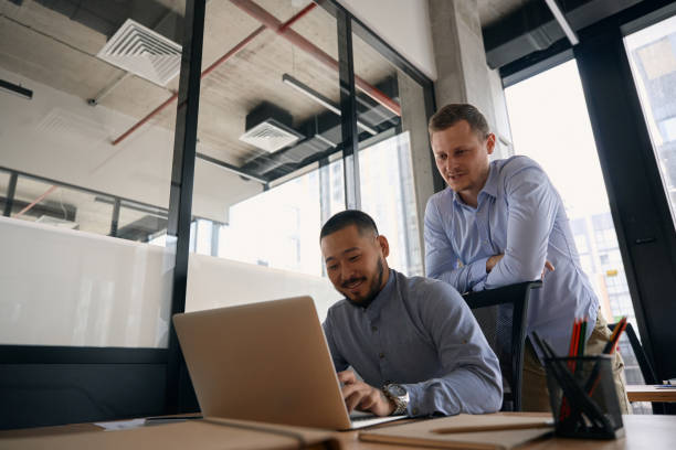 istock Corporate employee inputting information into laptop guided by coworker 1423054623