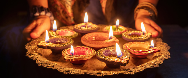 Diwali. Woman holding a tray with Diya oil lamps lit, Deepavali celebration. Hindu Festival of lights outdoors, India streets.