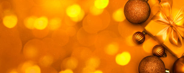 istock Christmas decorative composition with golden colored shiny Christmas balls and gift on bright yellow orange bokeh lights  background. Christmas or New Year concept. Festive Christmas background with baubles and copy space.  Banner. 1423058146