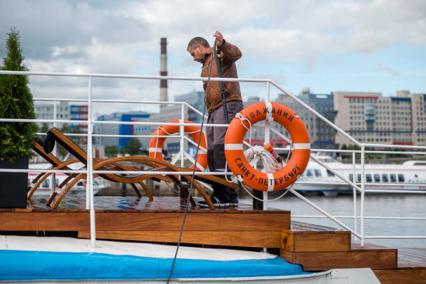 Russia, Saint Petersburg, September 10, 2022: A man washes the deck of a yacht with a hose