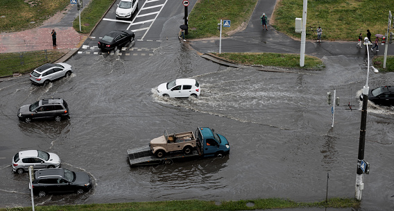 Minsk, Belarus, August 2022 - Cars are driving on a road flooded with heavy splashes of rainwater. climate change