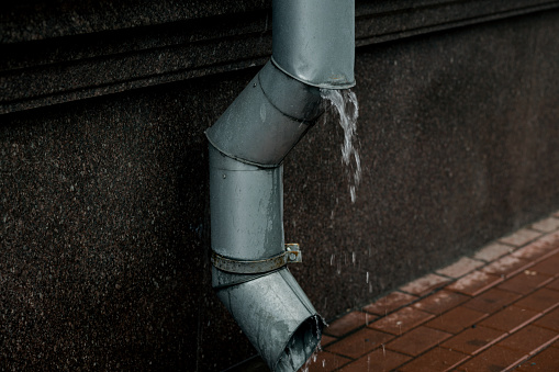 Rain water flowing from drainpipe, wet sidewalk closeup.
