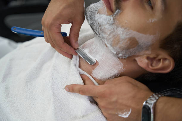 Cropped close-up photo of barbershop client looking relaxed while getting a shave from a hair salon specialist with straight razor