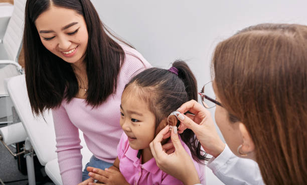 audiólogo cabe aparelho auditivo no ouvido da menina asiática enquanto visitava clínica auditiva com a mãe. soluções auditivas para crianças - hearing aid audiologist audiology small - fotografias e filmes do acervo