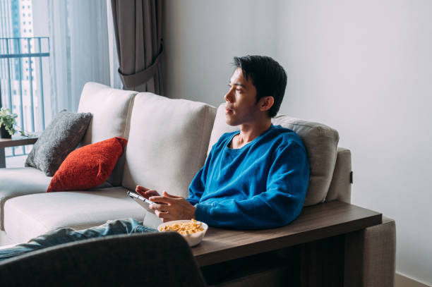 istock Smiling young Asian man relaxing and using tablet on couch. Looking Away 1423077921