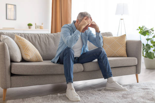 istock Stressed mature man sitting on couch grabbing head 1423077971
