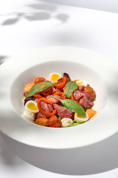 istock Salad with roast beef, vegetables and eggs on white table with harsh shadows. Steak salad in modern style with shadows of leaves. Flashy food. Meat salad with pastrami in summer menu. 1423081046