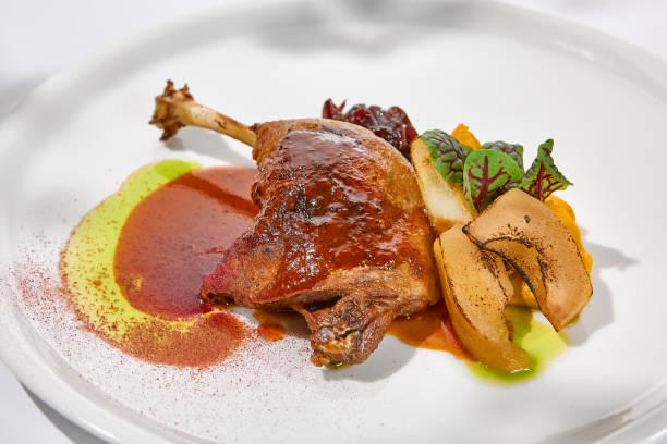 plat traditionnel français - confit de canard avec pomme cuite au four sur fond clair avec des ombres de soleil. cuisse de canard rôtie avec fruits et sauce sur assiette blanche en été dîner élégant cuisse rôtie - confit photos et images de collection