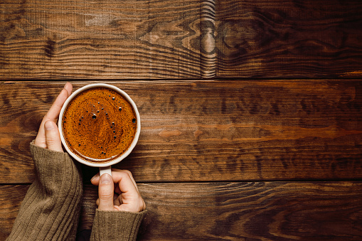 Hands with cup of coffee on dark wooden background with copy space. Top view, flat lay