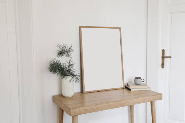 Christmas Scandinavian interior. Blank vertical wooden picture frame mockup. Pine tree branches in vase, cup of coffee and old books on table, desk. White wall background, doors. Empty copy space. stock photo