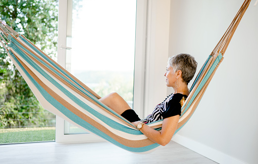 Smiling mature woman lying in a hammock hanging in a sun room at home on a summer afternoon