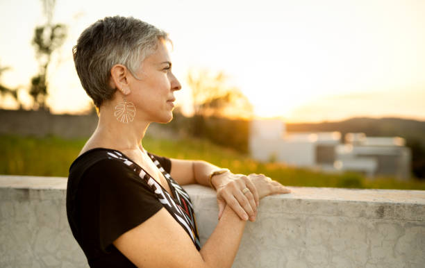 Mature woman leaning on a wall outside at sunset