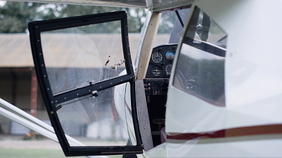 Professional pilot taking seat cabin white private airplane on aerodrome. Man aviator entering in ultralight aircraft before sky flight. Aviation engineer sitting cockpit to drive air transport.