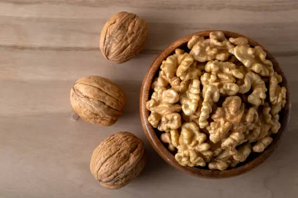 Peeled walnuts and whole walnuts on wooden background