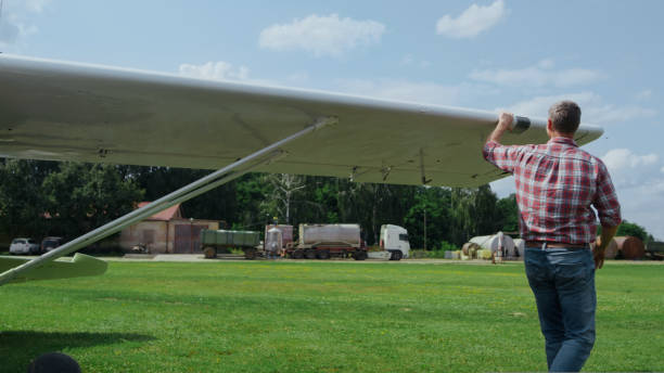 Aviator checking small plane before flying countryside aerodrome runway. Professional aviation engineer inspecting airplane fixing wings for long flight trip sunny day. Aircraft maintaining concept.