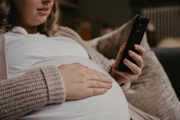 istock Pregnant woman siting on her sofa using her cellphone 1423115617