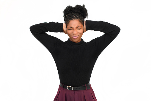 Annoyed African American woman in studio. Female model in black long sleeve shirt and trousers covering ears and closing eyes. Portrait, studio shot, emotion concept