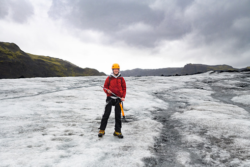 Teenage Boy with ice climbing gear standing on Glacier smiling at camera Sólheimajökull Glacier Southern Iceland