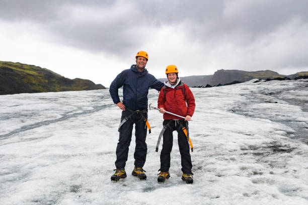 Father and Son with ice climbing gear standing on Glacier smiling at camera stock photo