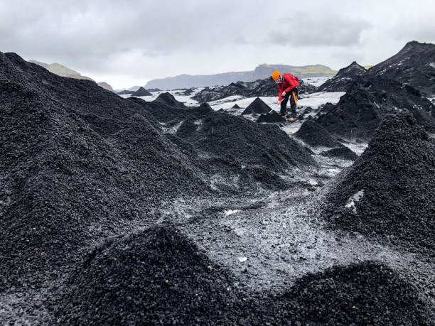 istock Young male standing between Lava Ash Ice Pyramids on a Glacier hitting away with ice axe 1423122117