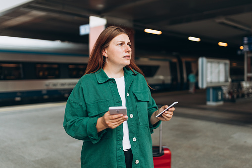 Joven refugiada pelirroja llorando y esperando el tren en el andén de la estación, perdió y usó un teléfono inteligente. Concepto de transporte ferroviario, Traveler. photo