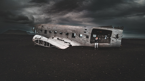Teenage male sitting in the Wrecked DC-3 Plane on Sólheimasandur with dramatic sky Sólheimasandur Solheimafjara Southern Iceland